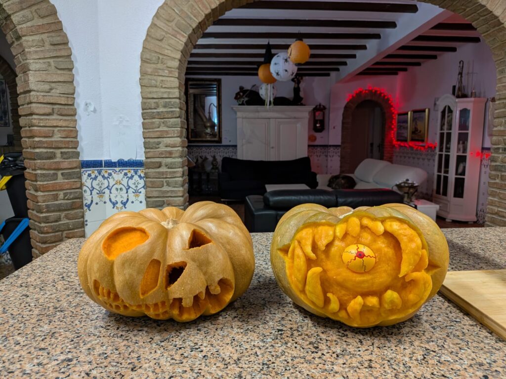 two pumpkins carved for halloween in a kitchen and living room area that is decorated for halloween. 